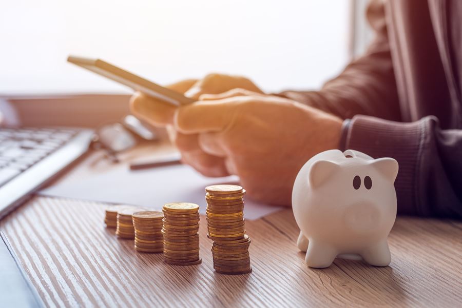 Man using phone behind a stack of coins and piggy bank